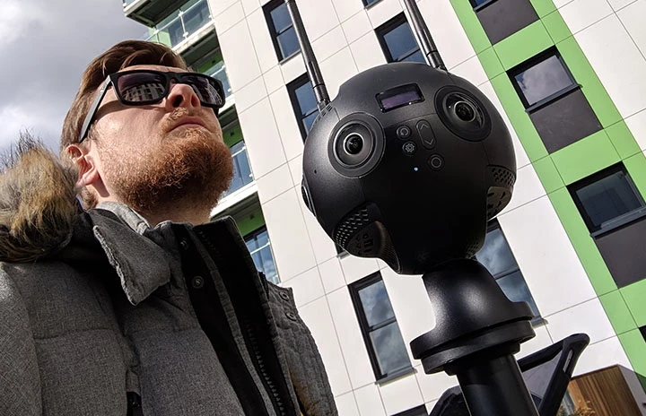 A man in a thick coat adjusting a 360 degree camera