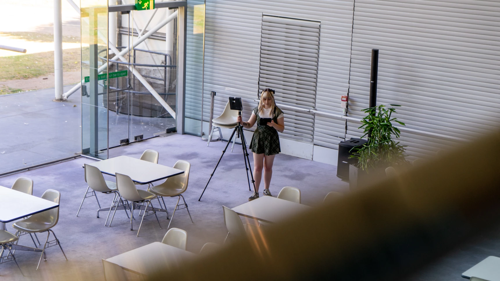A woman is scanning a space using a 360 camera, she is seen from a balcony looking ta an ipad